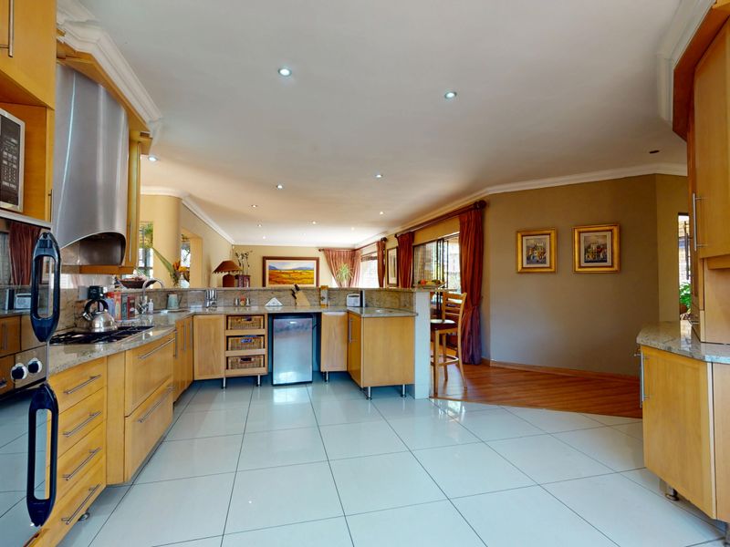 Spacious open-plan kitchen featuring light wood cabinetry, granite countertops, integrated appliances, and tiled flooring, flowing into the adjacent living area.