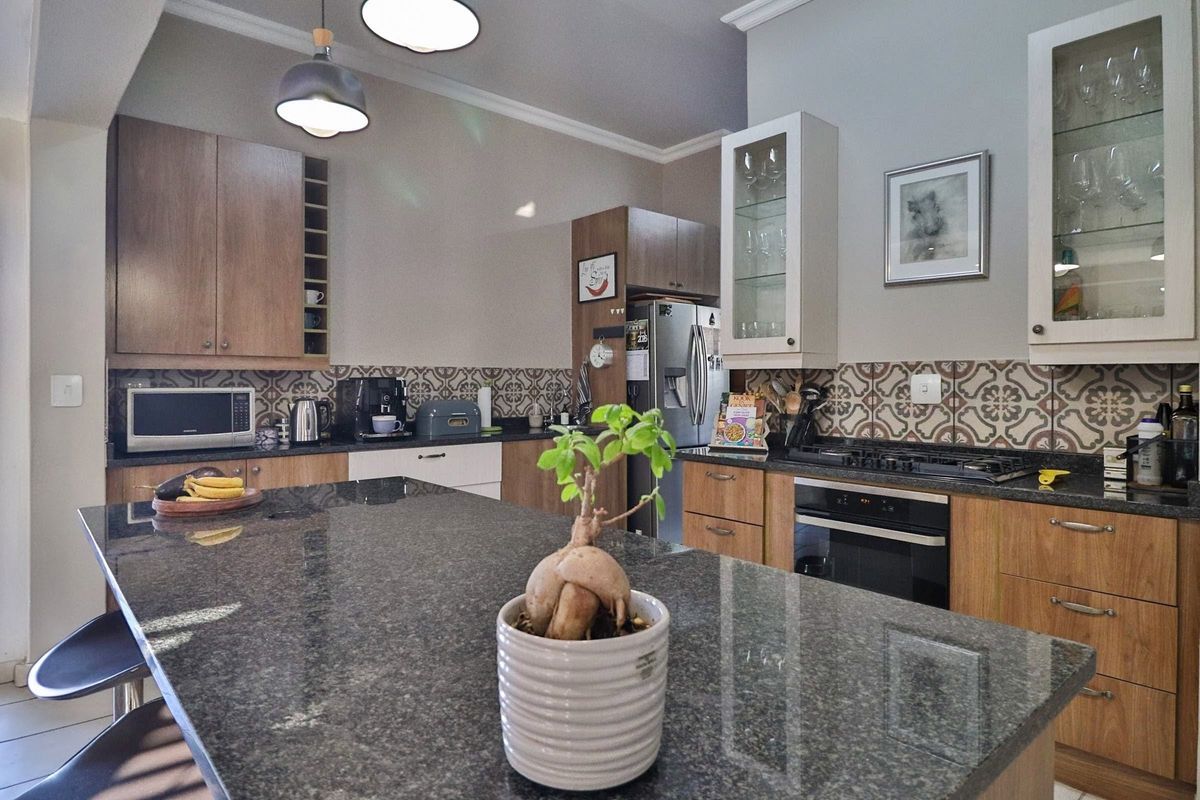 A well-appointed kitchen featuring granite countertops, a central island, built-in oven with gas hob, and stylish patterned tile backsplash with ample wooden cabinetry.