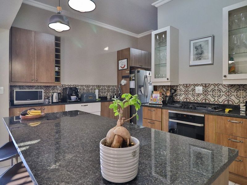 A well-appointed kitchen featuring granite countertops, a central island, built-in oven with gas hob, and stylish patterned tile backsplash with ample wooden cabinetry.