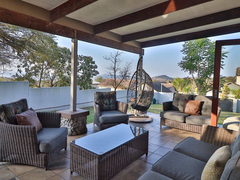 A covered outdoor patio featuring tiled flooring, exposed timber beams, and a stone-clad pillar, offering a pleasant space for relaxation with garden views.