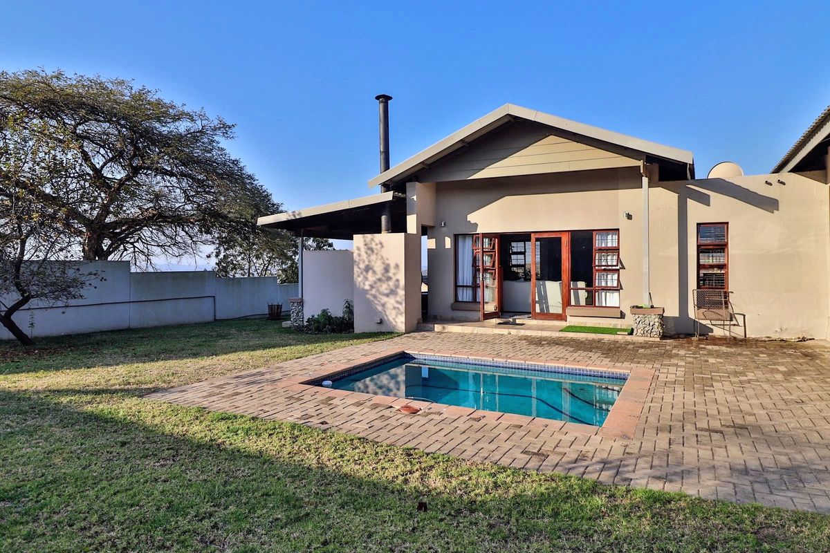 Rear view of the property featuring a paved patio area, a swimming pool, and an external fireplace chimney set within a private garden.