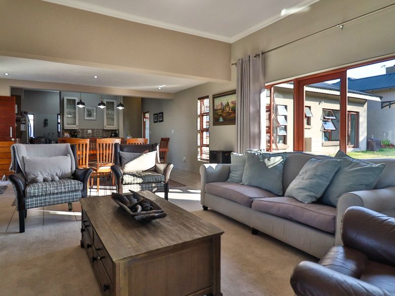 Spacious open-plan living and dining area featuring tiled and carpeted flooring, recessed lighting, and large timber-framed windows overlooking the rear garden.