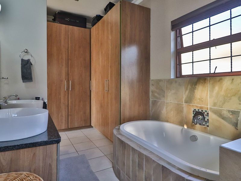 Bathroom featuring dual vanity basins, a tiled bathtub surround, and ample built-in cupboard storage space.