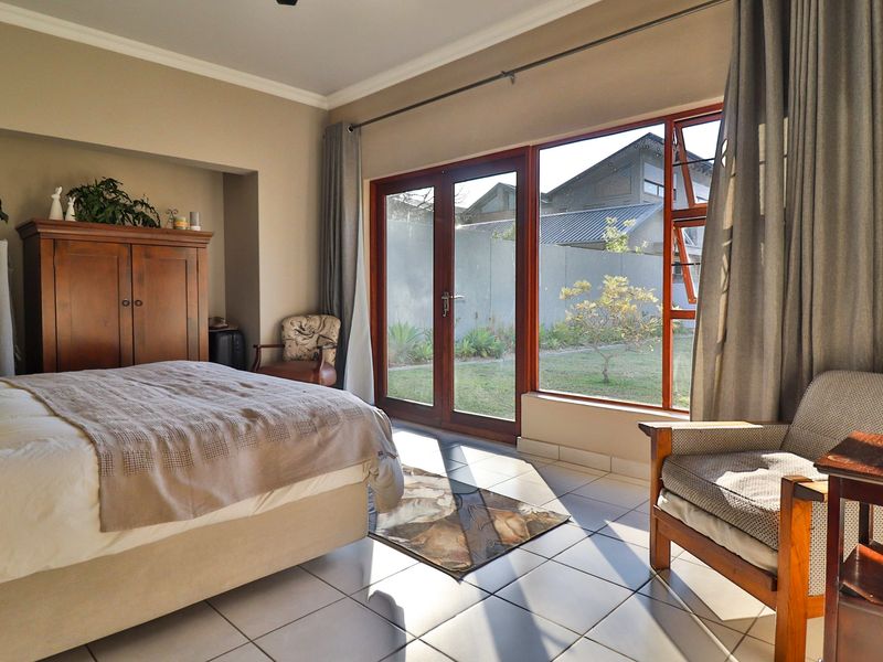 Spacious bedroom featuring tiled flooring, a recessed wall niche, and large glass doors providing direct access to the garden.