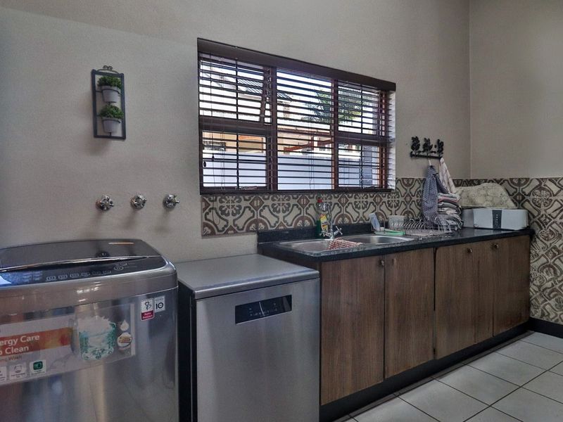 Functional laundry room featuring built-in cabinetry, granite countertops, a stainless steel sink, and decorative tiled backsplash with tiled flooring.