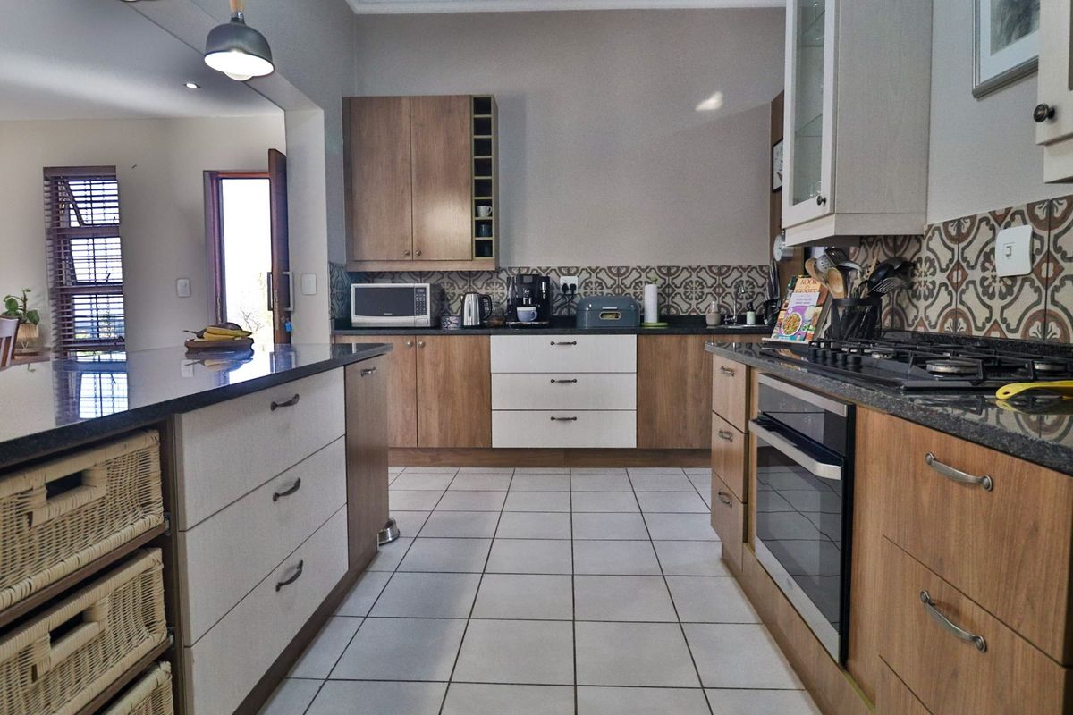 Modern kitchen featuring granite countertops, a central island, built-in oven with gas hob, and stylish patterned tile backsplash.