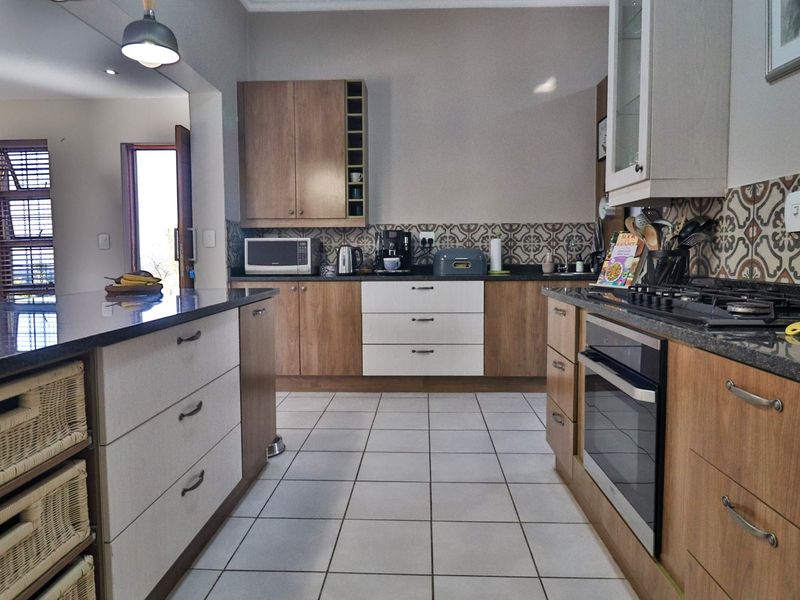 Modern kitchen featuring granite countertops, a central island, built-in oven with gas hob, and stylish patterned tile backsplash.