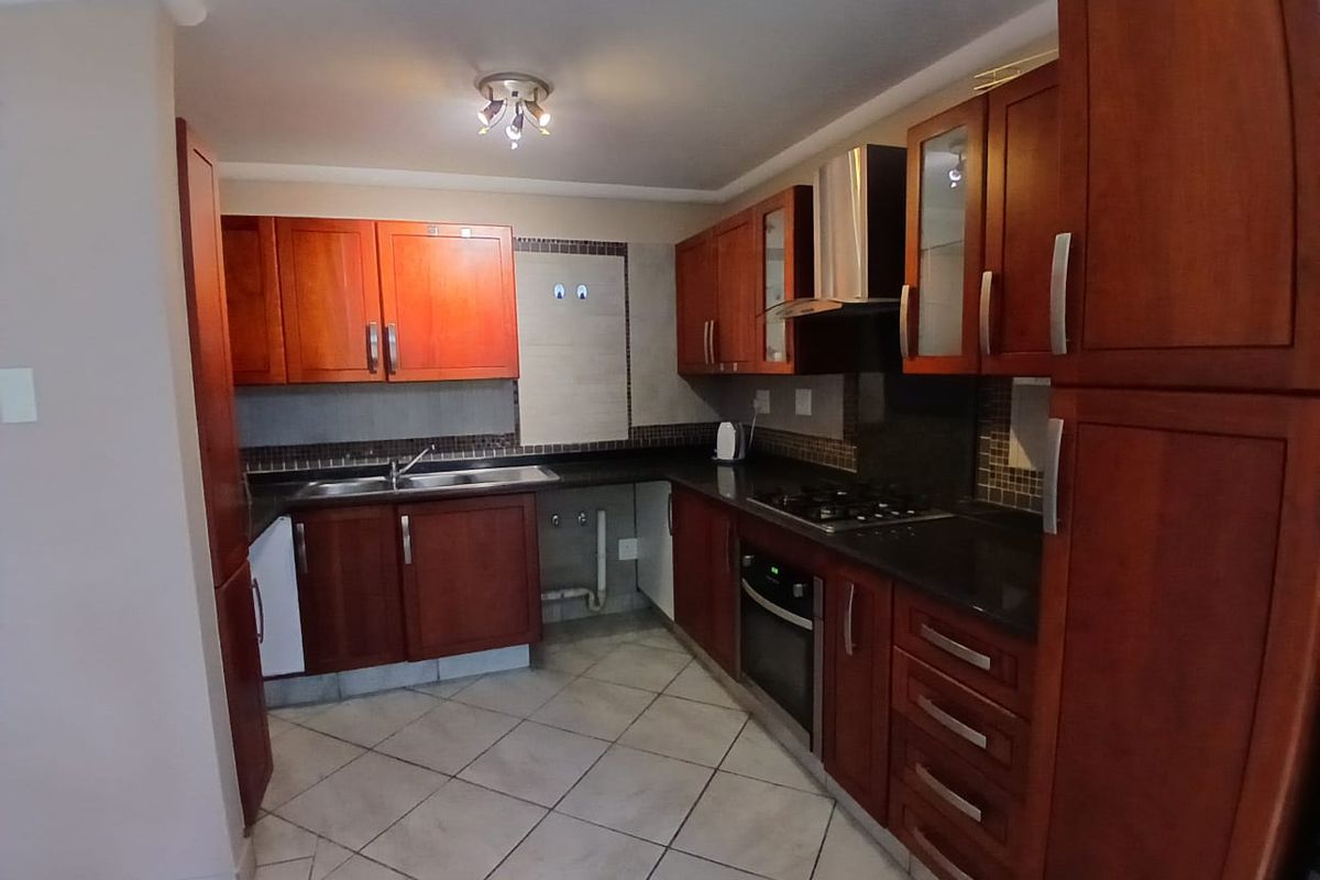 A functional kitchen featuring cherry wood cabinetry, granite countertops, a built-in oven, gas hob, and tiled flooring with a mosaic backsplash.