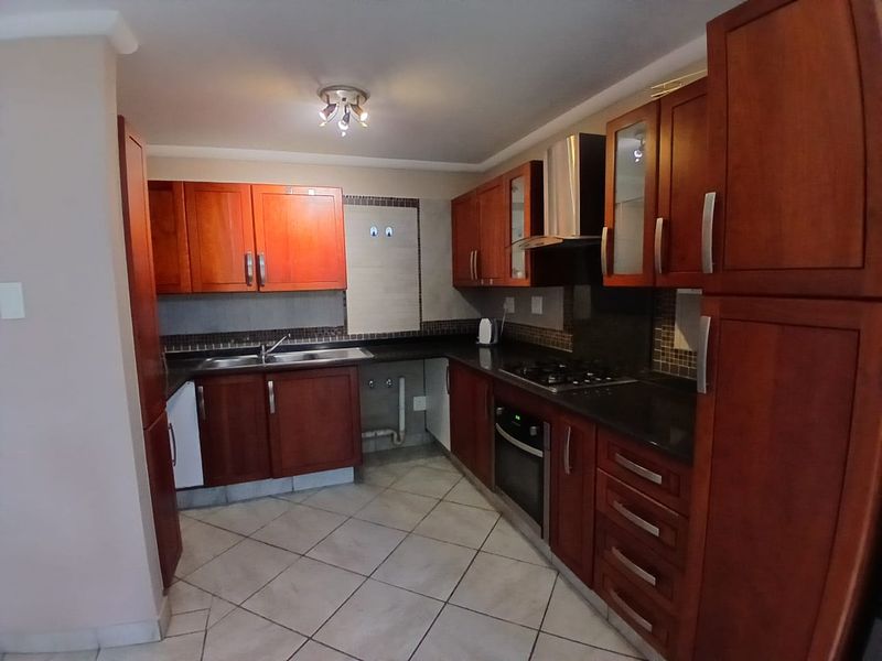 A functional kitchen featuring cherry wood cabinetry, granite countertops, a built-in oven, gas hob, and tiled flooring with a mosaic backsplash.