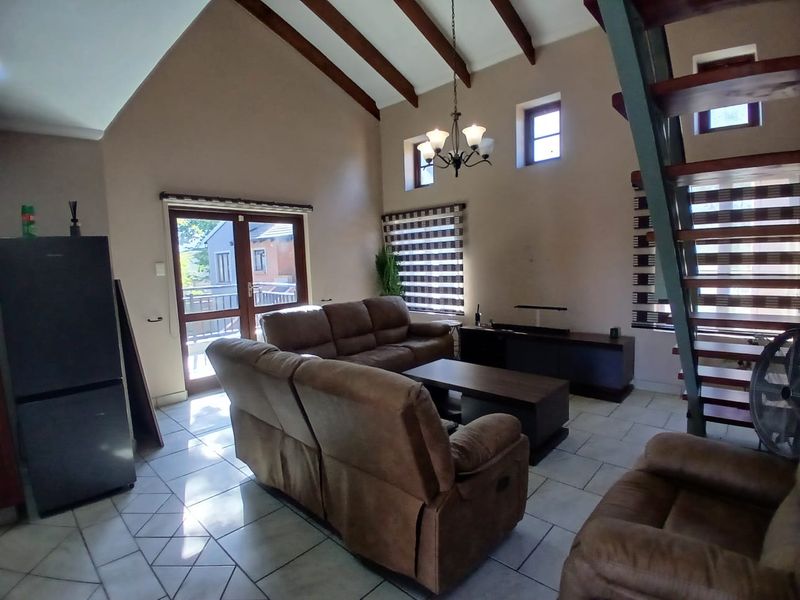 Spacious living room featuring a vaulted ceiling with exposed timber beams, tiled flooring, and a staircase leading to an upper level.
