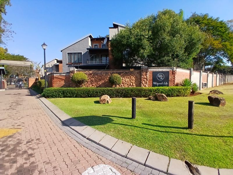 Front entrance view of the Wedgwood Lofts townhouse complex, featuring a stone boundary wall, manicured lawn, and paved driveway access.