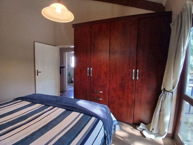 A bedroom featuring a large built-in wooden wardrobe, exposed ceiling beam, and direct access to an en-suite bathroom.
