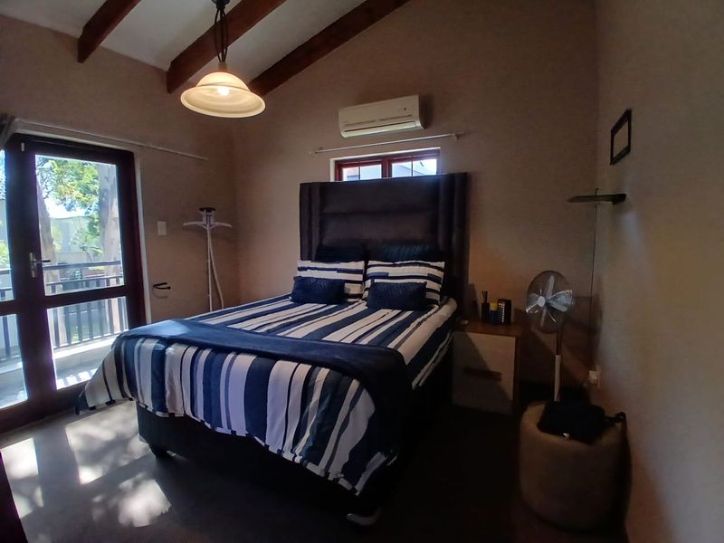 A cozy bedroom featuring exposed timber ceiling beams, a split-system air conditioner, and direct access to an outdoor balcony through a glass door.