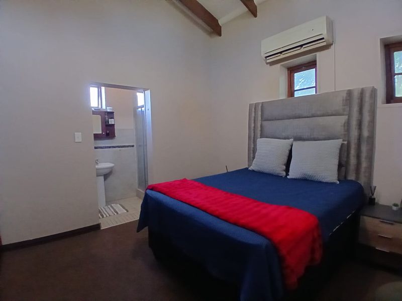 A bedroom featuring exposed timber ceiling beams, an air conditioning unit, and an adjoining en-suite bathroom with a pedestal basin and shower.