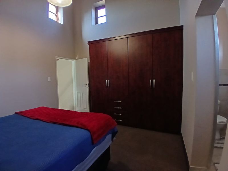 A bedroom featuring high ceilings, clerestory windows, and dark wood built-in cupboards, with an adjacent en-suite bathroom visible.