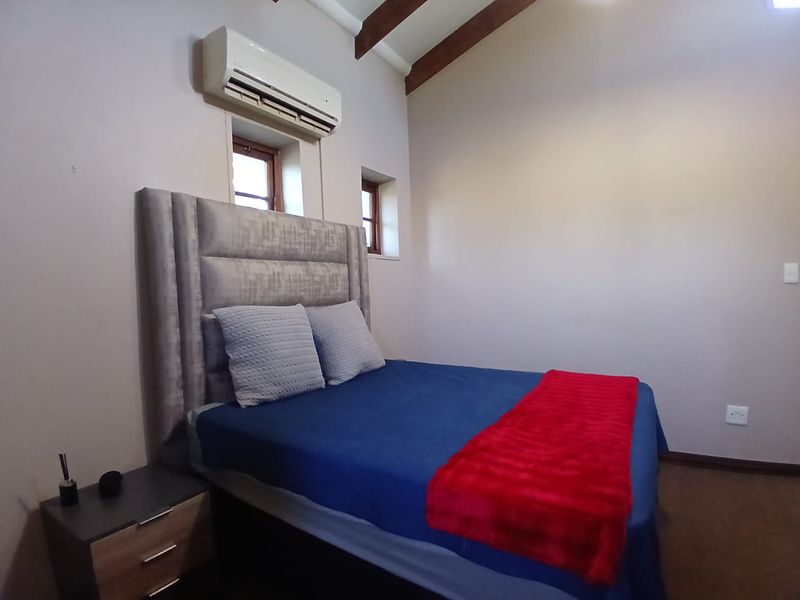 A cozy bedroom featuring exposed timber ceiling beams, a wall-mounted split-system air conditioner, and recessed windows.