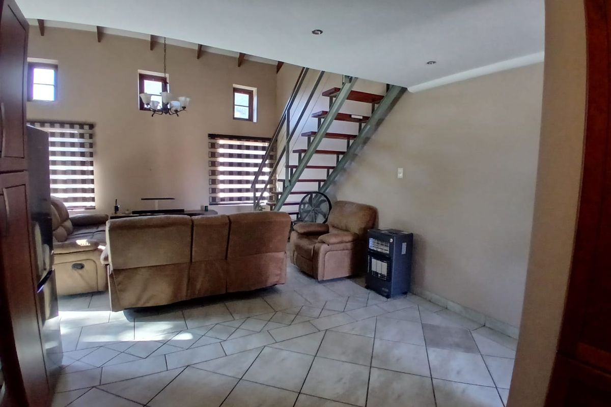 Spacious living area featuring high ceilings with exposed beams, tiled flooring, and a central staircase leading to the upper level.