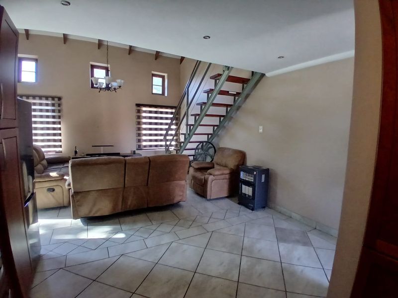 Spacious living area featuring high ceilings with exposed beams, tiled flooring, and a central staircase leading to the upper level.