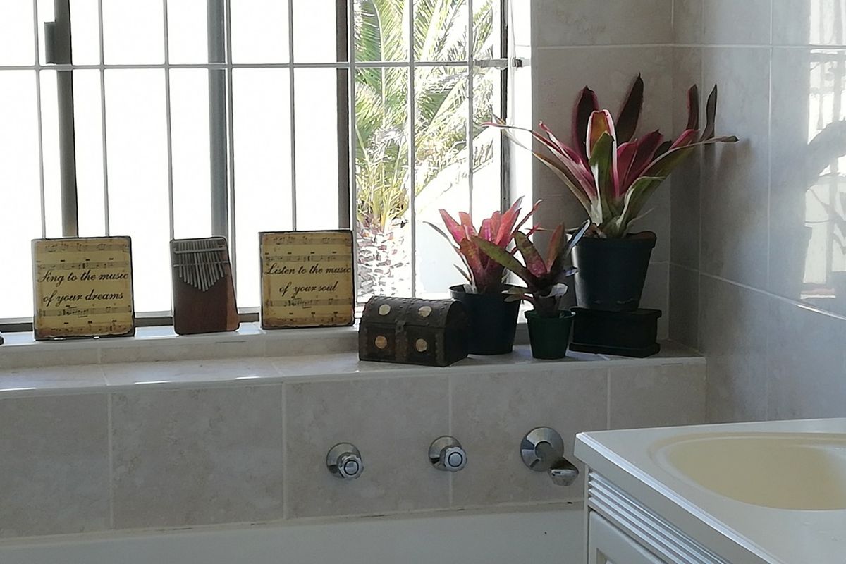 A bathroom featuring a built-in bathtub with chrome fixtures, tiled wall finishes, and a window with security bars.