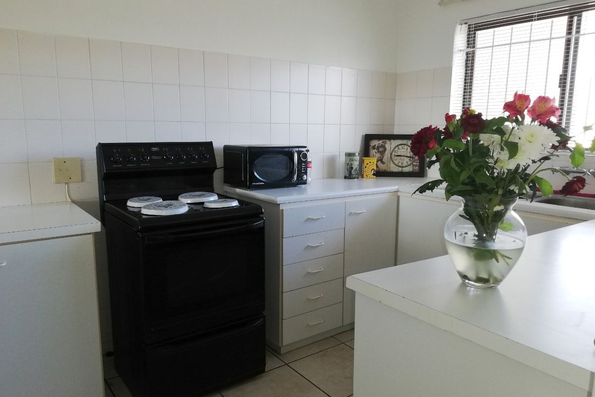 A functional kitchen featuring white cabinetry, laminate countertops, a tiled backsplash, and a freestanding stove, offering a clean and practical workspace.