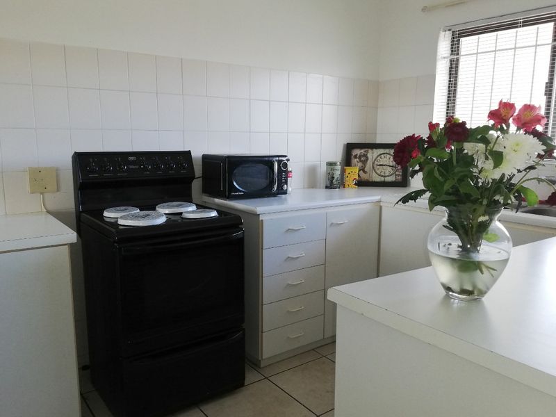 A functional kitchen featuring white cabinetry, laminate countertops, a tiled backsplash, and a freestanding stove, offering a clean and practical workspace.