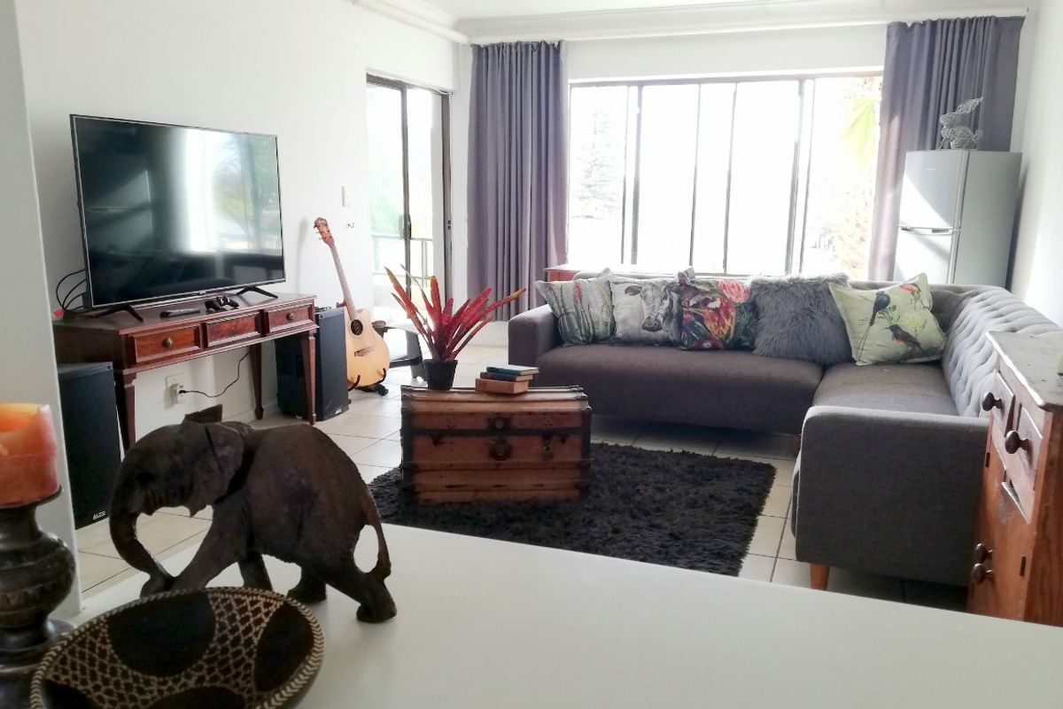 A bright living room featuring tiled flooring, large windows, and a sliding glass door providing access to the outdoor area.