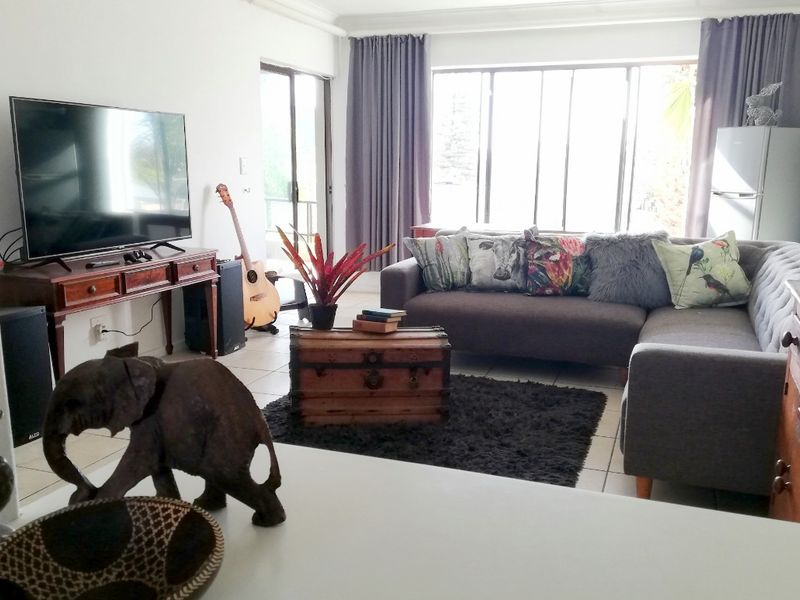 A bright living room featuring tiled flooring, large windows, and a sliding glass door providing access to the outdoor area.