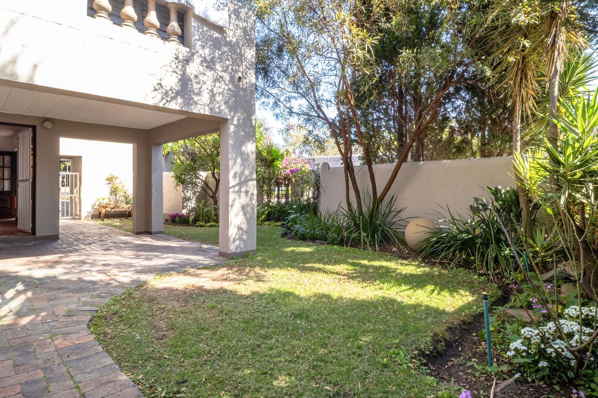 A private rear garden featuring a covered patio area with brick paving, established landscaping, and a secure boundary wall.
