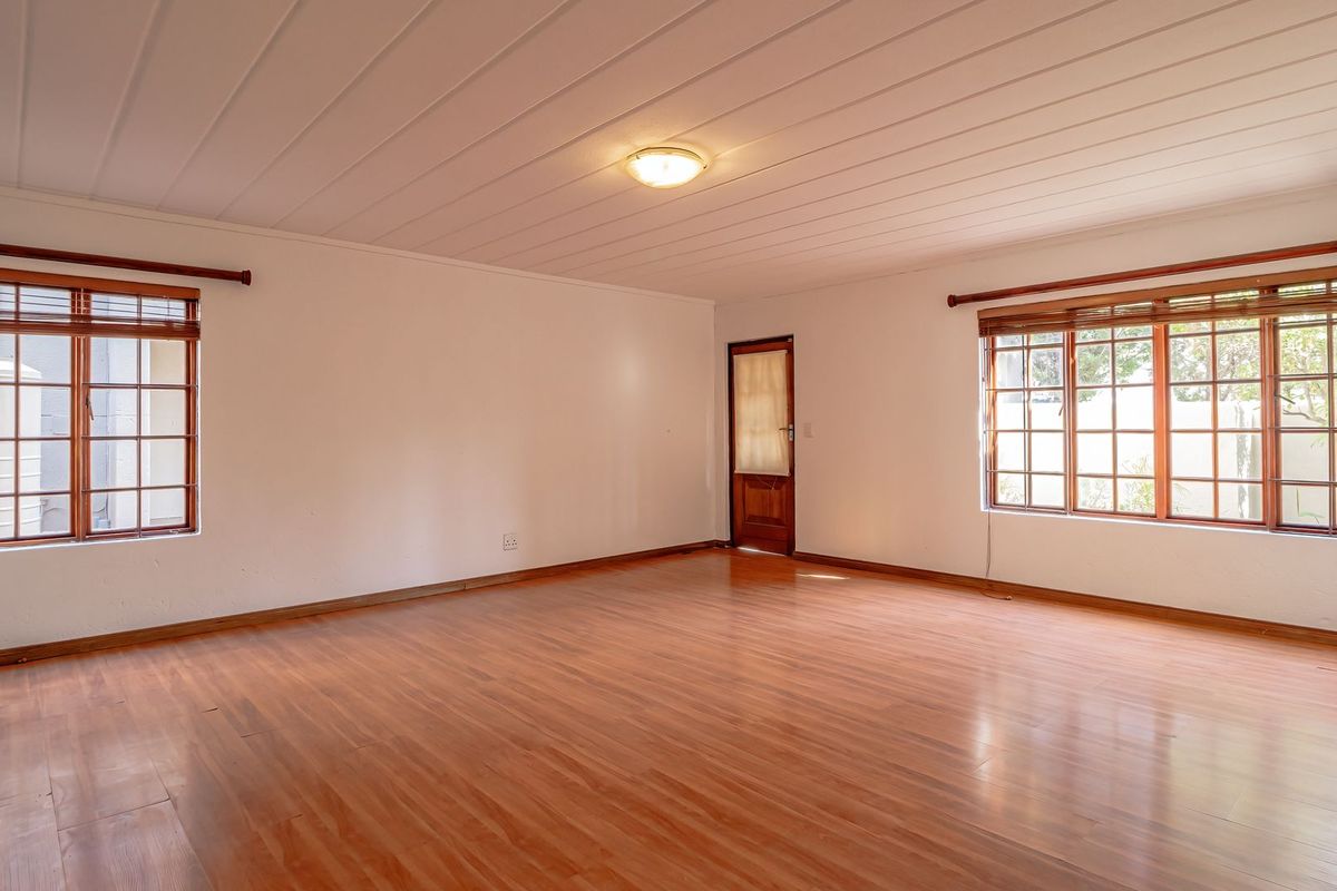 A spacious, empty living room featuring laminate flooring, timber-framed windows, and a paneled ceiling, offering a clean and neutral canvas for interior design.