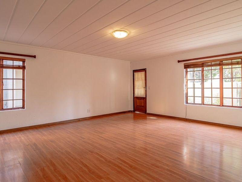 A spacious, empty living room featuring laminate flooring, timber-framed windows, and a paneled ceiling, offering a clean and neutral canvas for interior design.