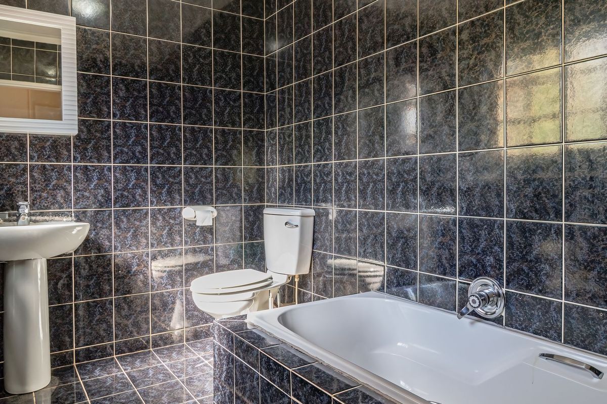 A bathroom featuring dark patterned wall and floor tiles, a white pedestal basin, a toilet, and a built-in bathtub.