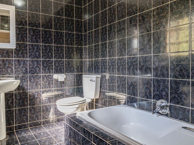 A bathroom featuring dark patterned wall and floor tiles, a white pedestal basin, a toilet, and a built-in bathtub.