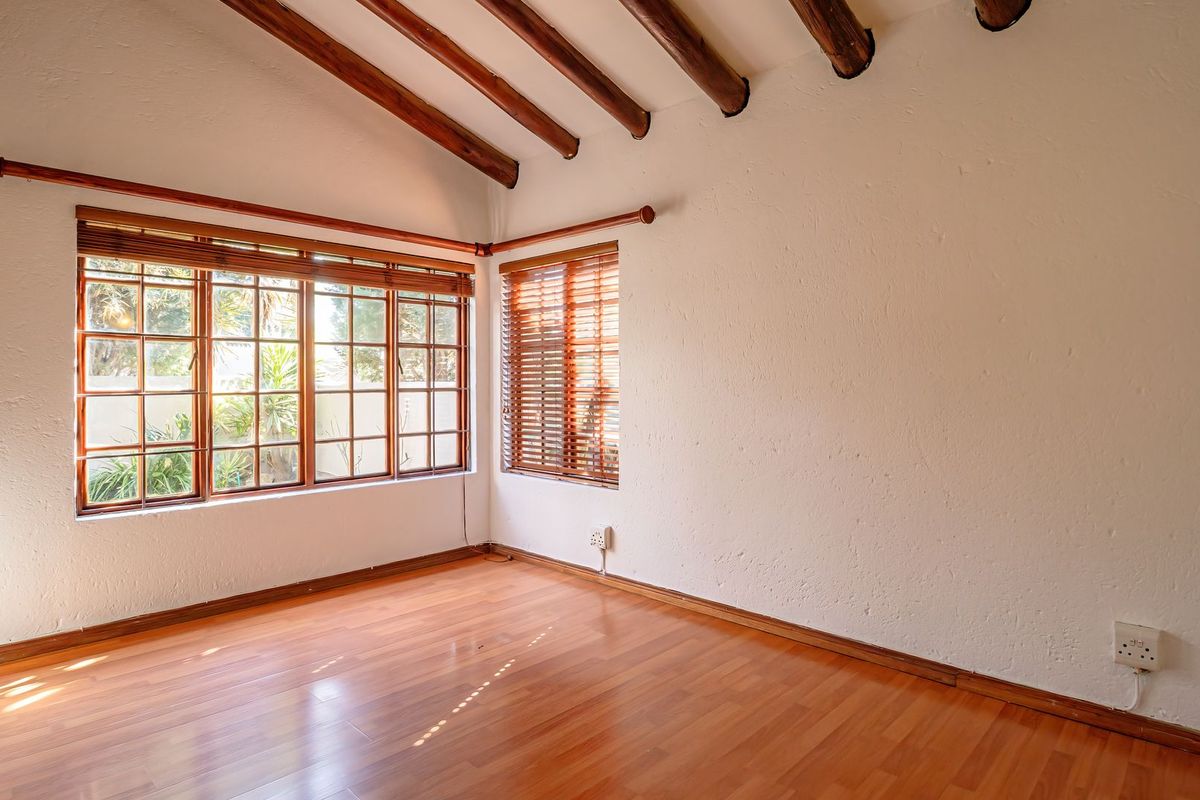 A bright, empty bedroom featuring exposed timber ceiling beams, laminate flooring, and large timber-framed windows with fitted blinds.
