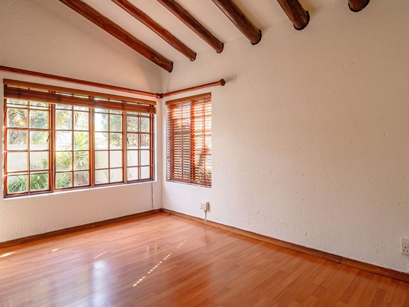 A bright, empty bedroom featuring exposed timber ceiling beams, laminate flooring, and large timber-framed windows with fitted blinds.