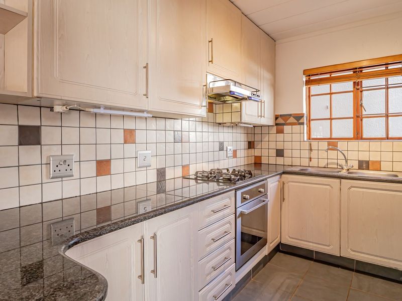A functional kitchen featuring light-toned cabinetry, granite countertops, a gas hob, built-in oven, and a tiled backsplash with a window for natural light.