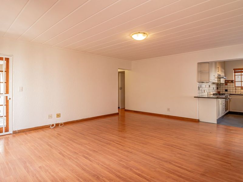 Spacious open-plan living area featuring laminate flooring and a functional kitchen with built-in cabinetry, oven, and hob, leading to an exterior security gate.