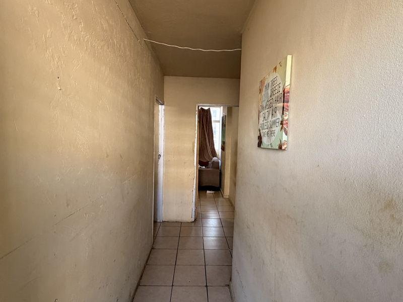 A narrow residential hallway featuring tiled flooring and plain wall surfaces, currently showing signs of wear and requiring cosmetic attention.