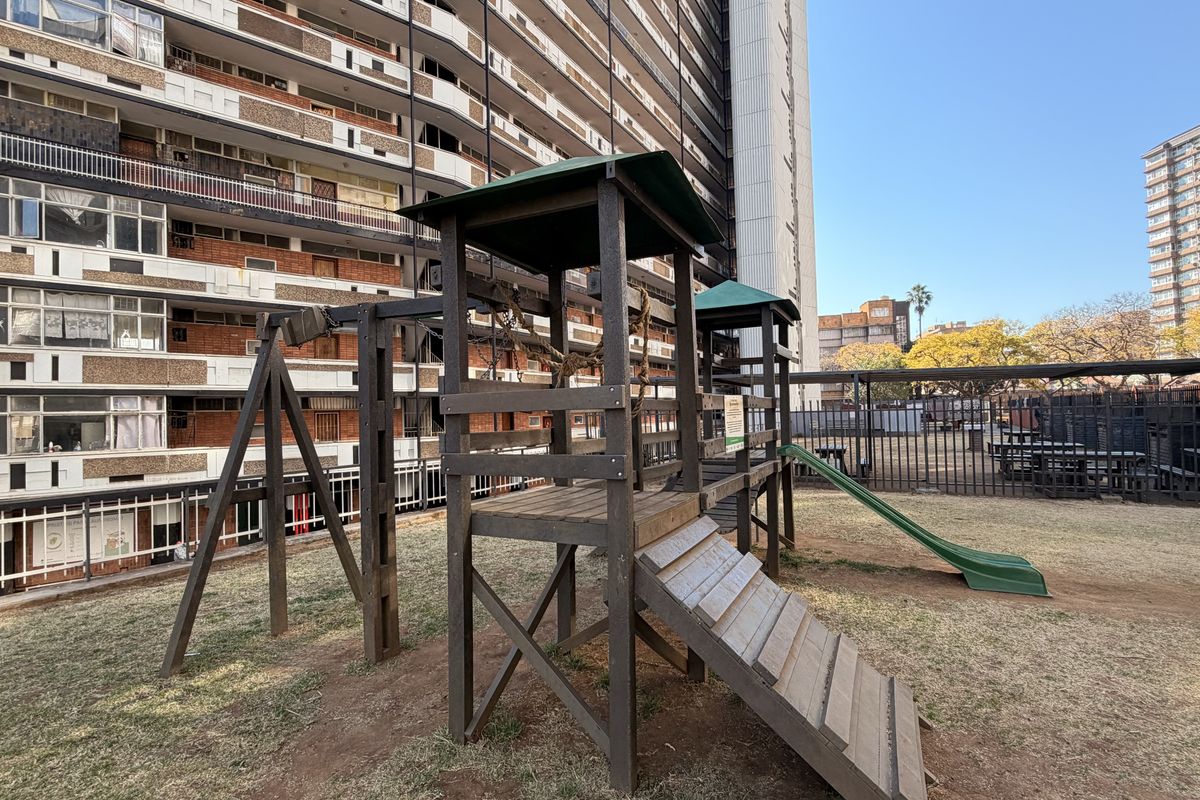 Communal outdoor area featuring a timber playground structure and metal perimeter fencing, situated within a high-density residential apartment complex.