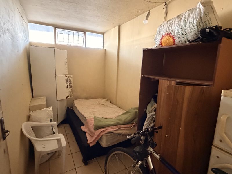 A small bedroom featuring tiled flooring and high-level clerestory windows, currently in need of cosmetic refurbishment and wall repairs.