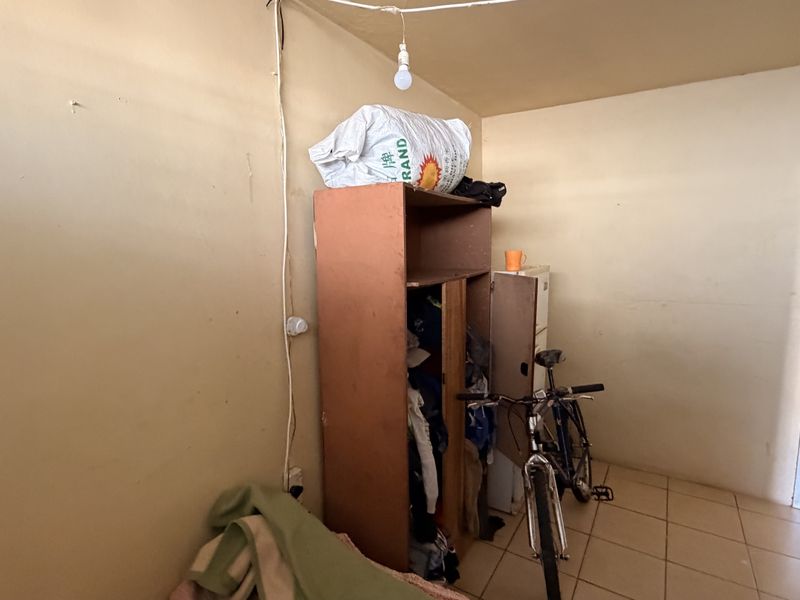 A small bedroom featuring tiled flooring and basic wall finishes, currently used for storage. The space requires cosmetic updates and improved lighting.