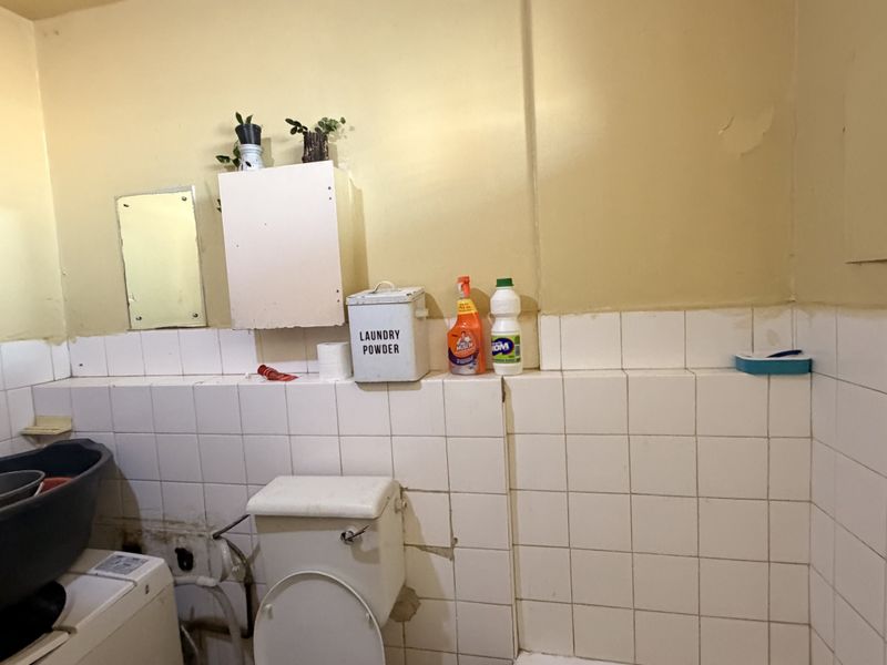 A functional laundry area featuring a toilet, wall-mounted cabinetry, and tiled splashbacks, currently showing signs of wear and requiring maintenance or renovation.