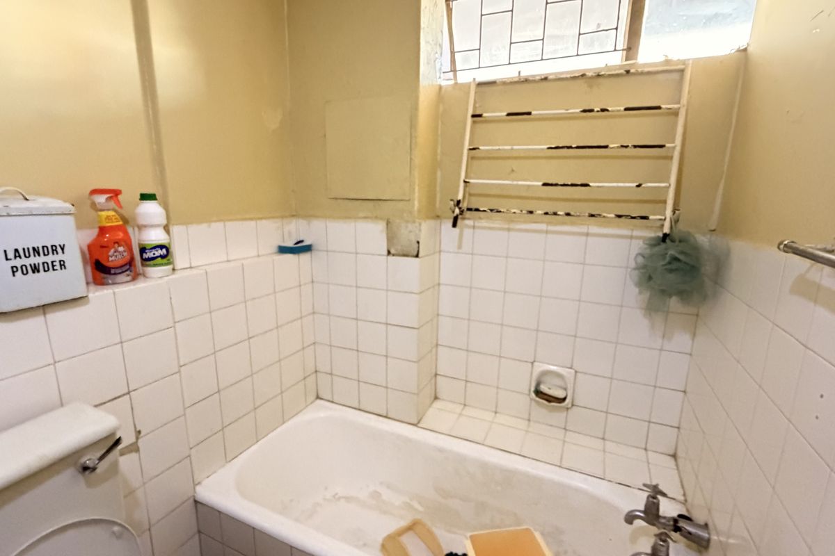 A dated bathroom featuring a bathtub with tiled splashback and a wall-mounted drying rack, requiring cosmetic updates and maintenance to improve its condition.