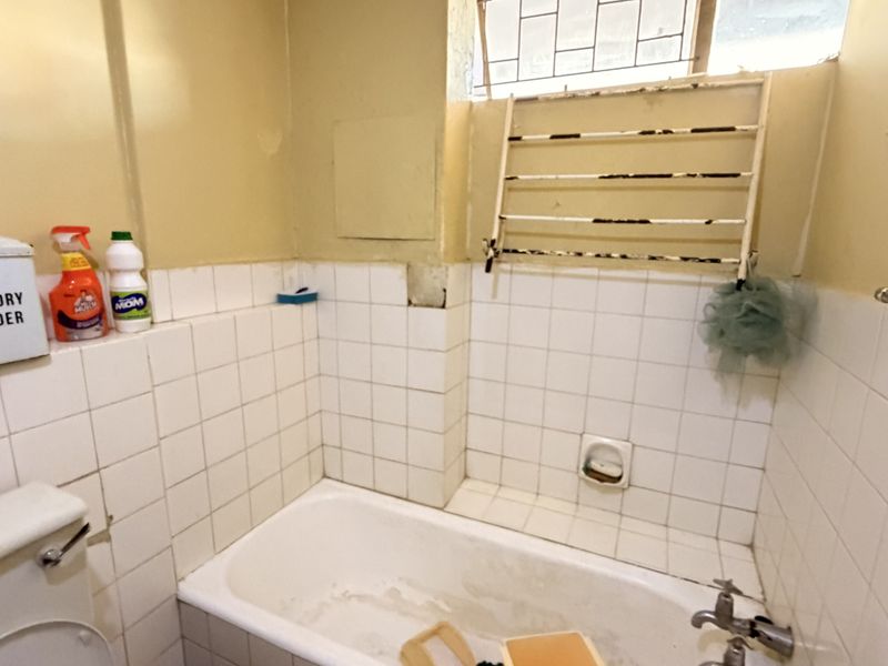 A dated bathroom featuring a bathtub with tiled splashback and a wall-mounted drying rack, requiring cosmetic updates and maintenance to improve its condition.