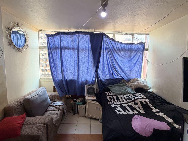 A bedroom featuring tiled flooring and a large window, currently requiring maintenance and cosmetic updates to the wall finishes and electrical fixtures.