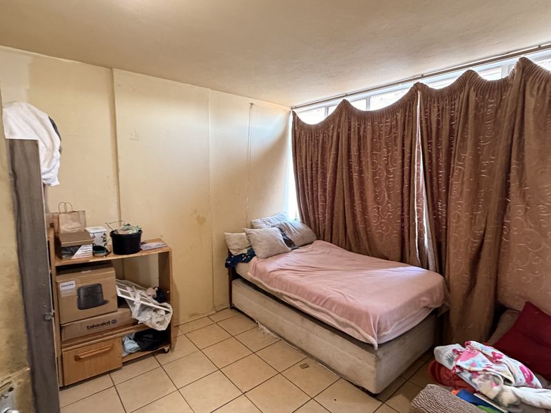 A bedroom featuring tiled flooring and a large window. The room requires cosmetic updates, including wall repairs and fresh paint to improve its overall condition.