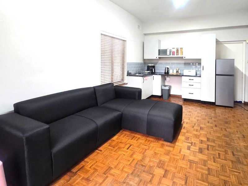 Open-plan living area featuring classic parquet flooring and a compact kitchen with white cabinetry and subway tile backsplash.