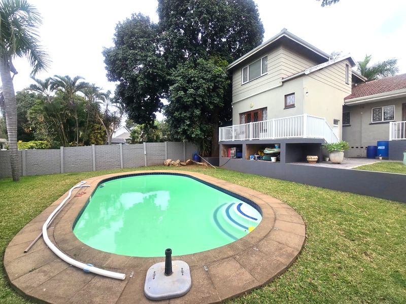Rear garden featuring a swimming pool with paved surround, a raised patio area with white railing, and perimeter precast concrete walling.