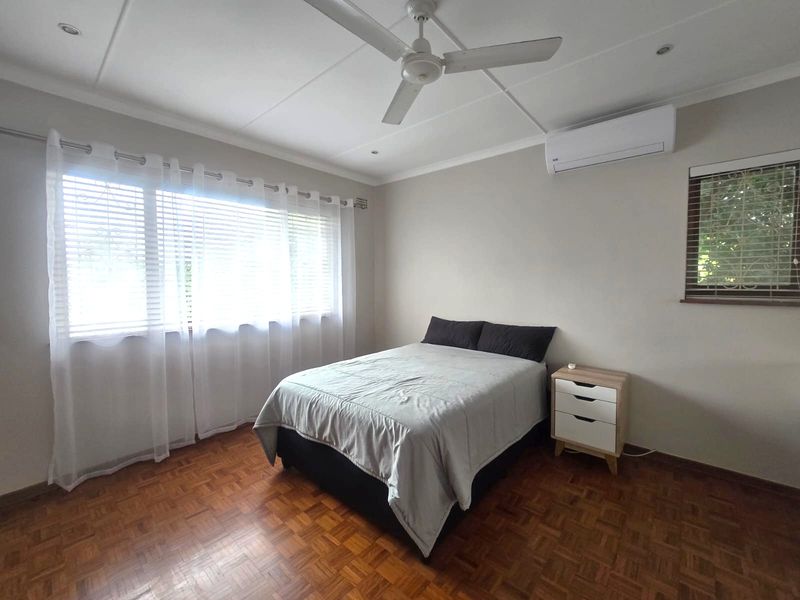 A well-maintained bedroom featuring classic parquet flooring, a ceiling fan, and a wall-mounted split-system air conditioner for climate control.