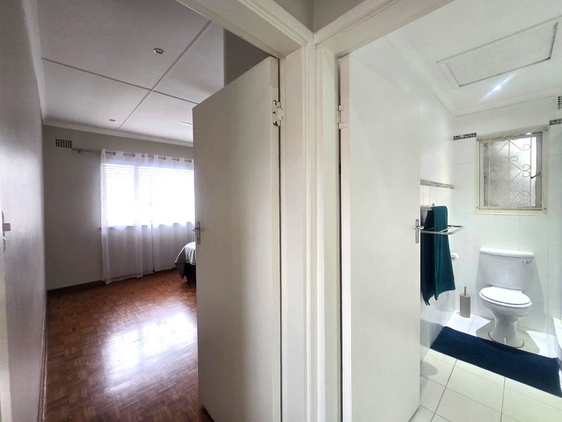 A view from the hallway looking into a bedroom with parquet flooring and an adjacent bathroom featuring tiled floors and a built-in toilet.