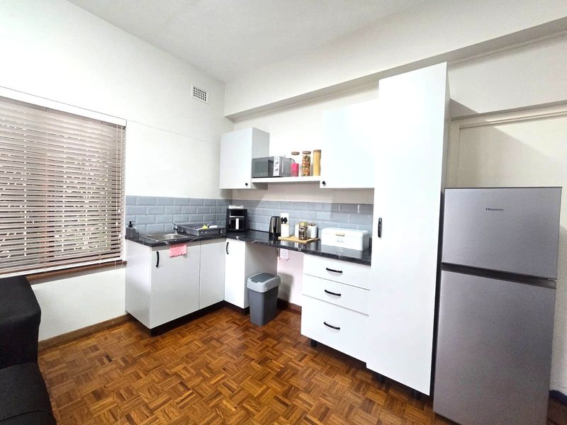 A functional kitchen featuring white cabinetry, dark laminate countertops, a subway tile backsplash, and classic parquet flooring.